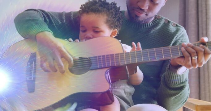 Father guiding baby's hands while baby reaching and strumming guitar at sound hole, teaching music