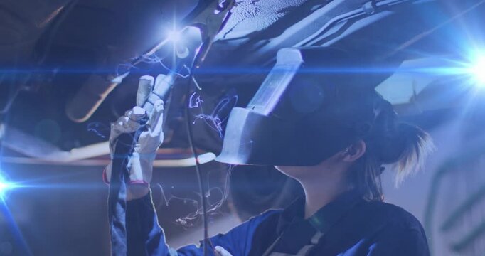 Female technician raising torch and initiating welding arc along panel seam, repairing underbody