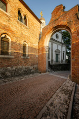 Naklejka premium Characteristic Italian cobblestone alley overlooked by an old house and a church passes through an arch. Udine, Friuli Venezia Giulia, Italy.