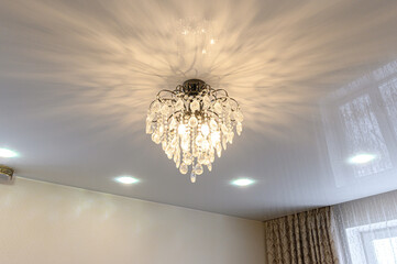 crystal chandelier with cascading droplets mounted on a satin stretch ceiling, complemented by...