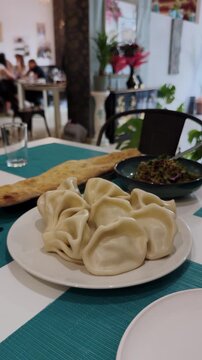 On the table at a Georgian restaurant is a jonjoli salad, hot khinkali, and Georgian lavash, fresh from the oven. Vertical video.