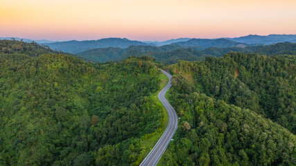 Fototapeta premium Aerial view of a scenic winding mountain road cutting through lush green hills in Nan, Thailand. The dramatic curves form the shape of the number three, making it a popular tourist attraction