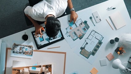 Top view of project manager writing house idea on sticky notes while looking plan at tablet. Aerial...