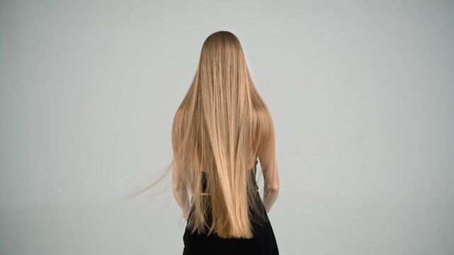 Blonde woman flipping long hair in slow motion, back view