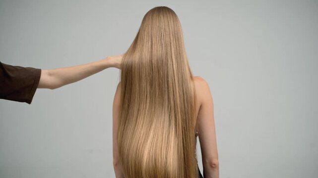 Stylist hand creating waves in long blonde hair, back view slow motion
