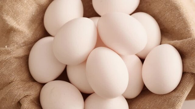 Gathered white eggs piled carefully inside a light tan woven cloth on a minimalist white backdrop
