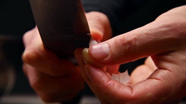 Chef slices garlic clove with knife, preparing ingredients on kitchen counter
