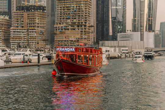 Traditional wooden dhow boat named Alexandra navigating through Dubai Marina with modern skyscrapers in the background
