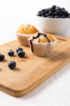 Two Homemade Blueberry Muffins on Bamboo Cutting Board with Fresh Blueberries