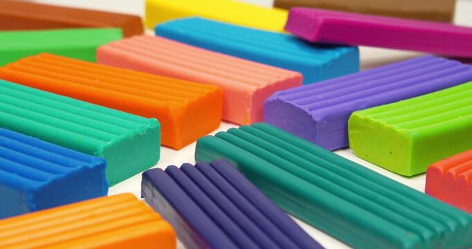 Multicolored pieces of plasticine for modeling rotate on a white table. Soft clay blocks for fun and skillful modeling. Colorful plasticine pieces ready for creative play