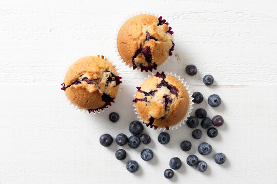 Overhead View of Three Homemade Blueberry Muffins with Fresh Blueberries on White Surface