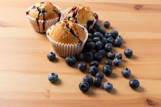 Three Homemade Blueberry Muffins with Scattered Fresh Blueberries on Wooden Table, Horizontal