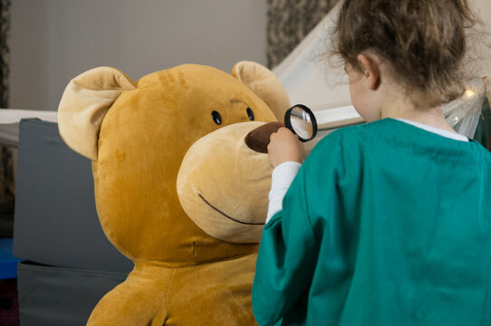 Junior doctor checking teddy bear nose with magnifier during pretend play