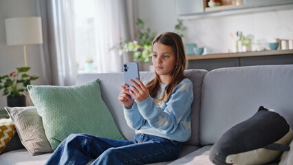 Obraz premium Carefree young lady browsing cellphone relaxing home sofa closeup. Teen girl