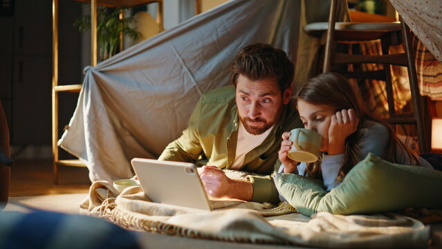 Parent child watching cartoons tablet lying blanker fort drinking tea closeup. 