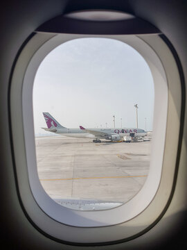 Doha, Qatar &ndash; February 5, 2026: View through airplane window showing Qatar Airways aircraft parked on the airport apron at Hamad International Airport with ground service equipment 