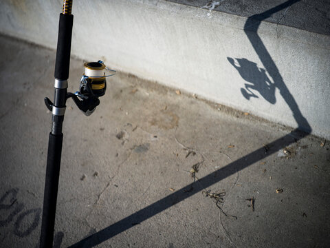 Fishing rod in the sun propped against a wall and fence