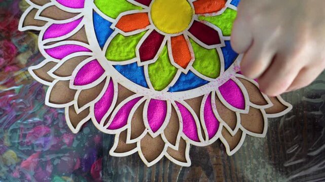 Top down flatlay of powder being poured using hand into template stencil with vibrant floral pattern on floor decoration for indian hindu festival like diwali holi