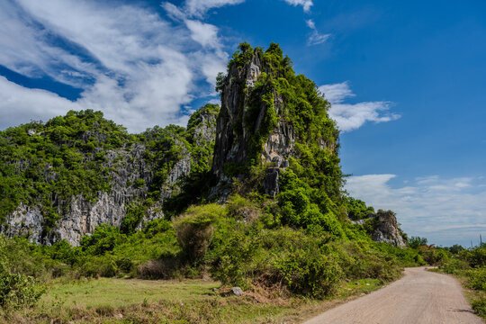 Dirt road beside lush limestone karst cliffs under blue sky