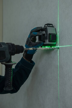 A man measures distances with a laser level and drills into a wall with a hammer drill.