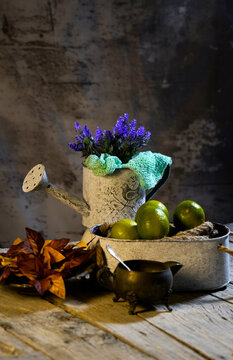 Natura morta con fiori di lavanda in annaffiatoio vintage e cesto di limoni su piano di legno antico.