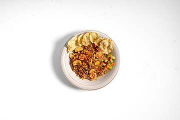 Fototapeta premium Top view of Indonesian shrimp fried rice served with crackers and fresh vegetable garnish on a plate isolated on white background.