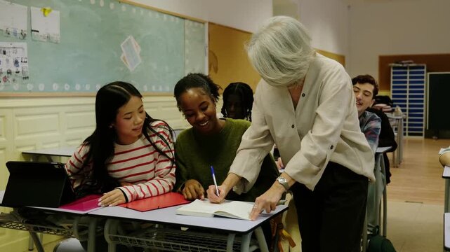 Senior teacher assisting a black and an asian student with their classwork during a lesson
