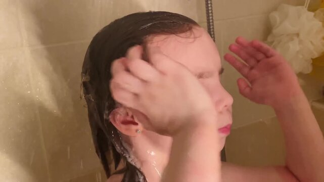 Close-up little girl bathing in a bathtub. Water and foam are visible as baby washes herself during a daily routine. Healthy childhood habits and self care development in domestic bathroom setting.