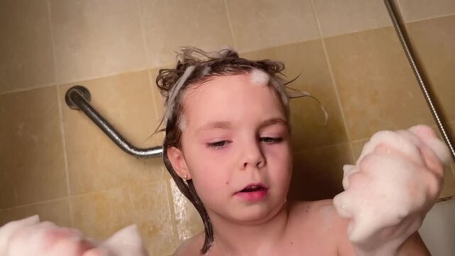 Close-up little girl bathing in a bathtub. Water and foam are visible as baby washes herself during a daily routine. Healthy childhood habits and self care development in domestic bathroom setting.