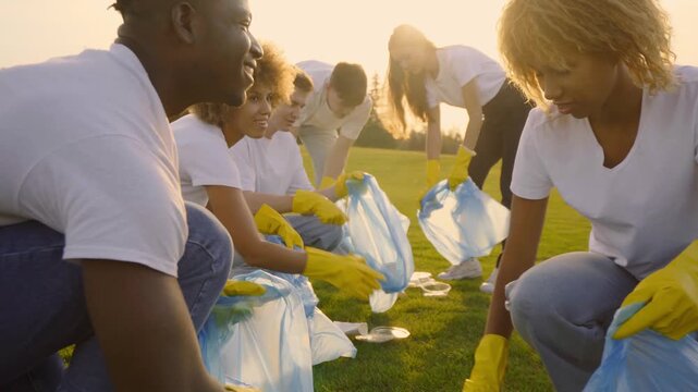 Multiracial group of six people volunteers with garbage bags to clean nature together in the park and talk about strategy outdoors at sunset golden light 4K UHD B-Roll footage