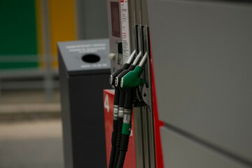 Fuel pump nozzles at urban station green and black hoses resting on metal dispenser beside trash bin, concrete forecourt and payment terminal, city © Alena