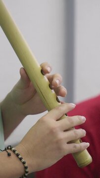 Vertical close-up shot focusing on the finger positioning of a musician playing a quena, a traditional Andean bamboo flute. The hands are shown with precision, covering the finger holes of the light-c