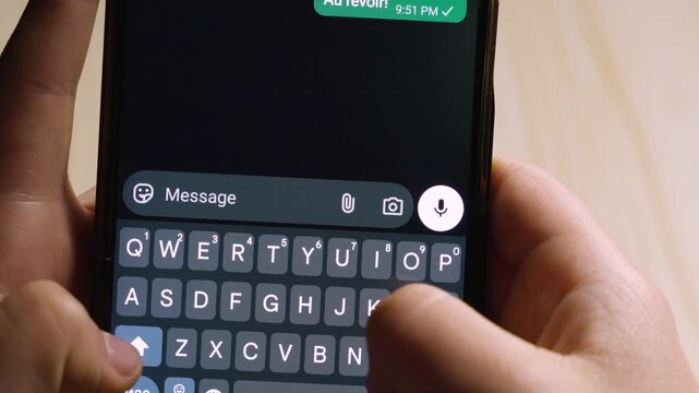 Close-up of hands typing the French farewell "Au revoir!" on a smartphone. Concept of ending a conversation and digital communication in a dark-themed interface.
