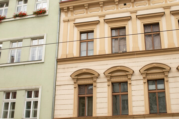 Fototapeta premium Paired pastel city facades with wires and balconies, green and beige stucco, rhythmic window alignment, visible cables cutting across sky, subtle
