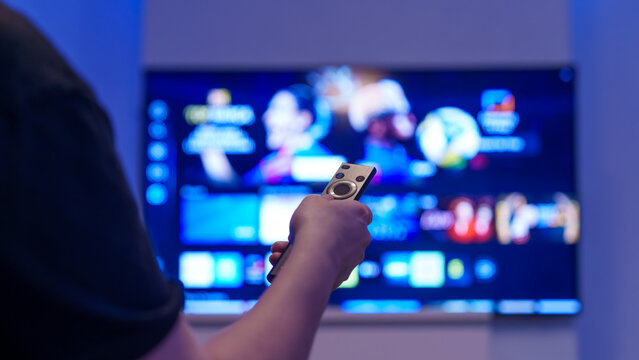Hand holding remote control toward smart tv streaming screen