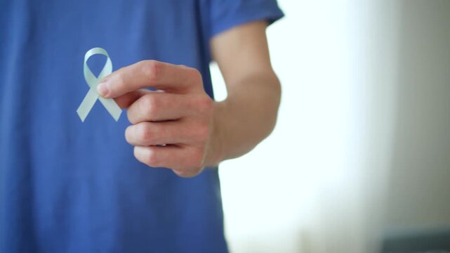 A man holds a blue satin ribbon in his hand, representing prostate cancer awareness, early detection, and support for patients and their families.