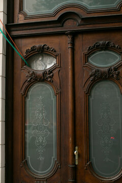 Carved wood door with oval etched glass and delicate filigree, urban storefront detail shows lacelike etching, warm grain and decorative molding