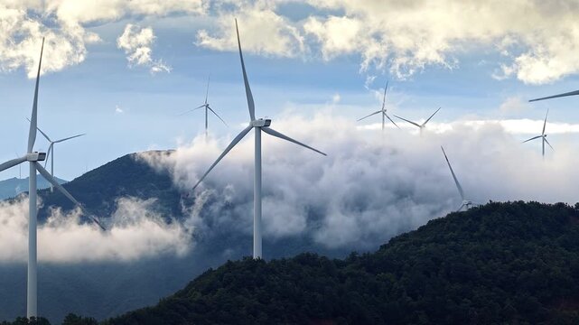 Wind turbines standing on mountain peaks above clouds at sunrise, generating renewable energy in Guilin, China.