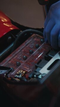 Close Up Woman in Protective Gloves Uses Screwdriver to Loosen Bolts on Battery Terminals of Motorcycle. Precision of Electrical Service and Approach to Bike Repair in Garage Setting. Vertical Shot.