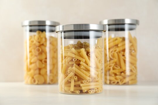 Different types of pasta in jars on white wooden table, closeup