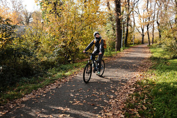 Woman riding bicycle along autumn park path surrounded by golden trees. Active lifestyle and eco friendly transport concept.