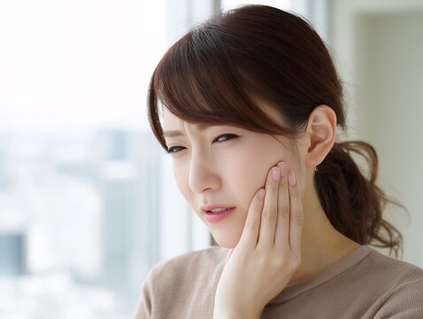 奥歯の痛みや知覚過敏に悩み頬に手を当てて顔をしかめる茶髪でポニーテールの若い女性