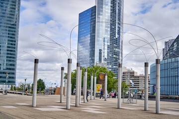 Contemporary urban plaza with modern art installation of tall white cylindrical poles and curved metal wire structures in Paris La Défense business district © Andrius