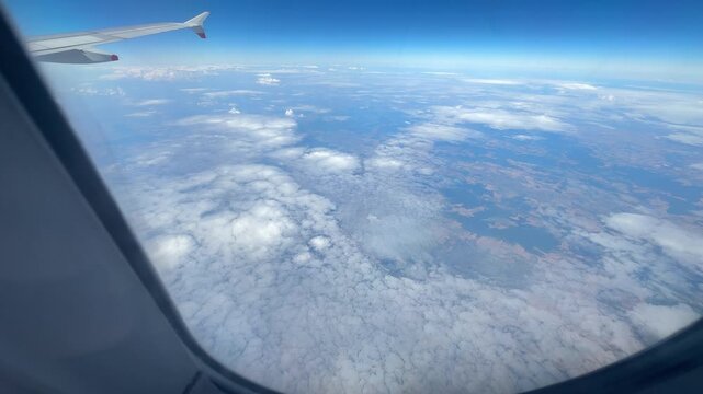 High altitude aerial video from an airplane window looking down at patchy white clouds casting shadows over rural countryside fields.