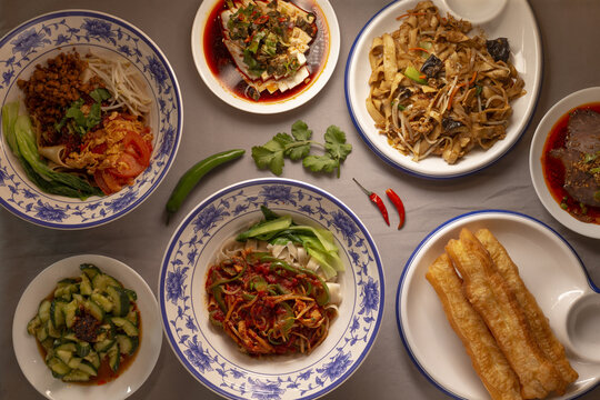 Close-up of Chinese cuisine dishes arranged on a dining table. Several plates with prepared meals are placed together for serving. Cilantro and cilli pepper, hand-made pasta in plate.