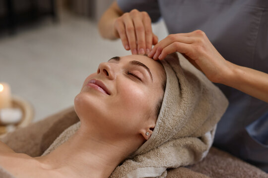 Beautiful woman wrapped in towel receiving facial massage on couch indoors, closeup
