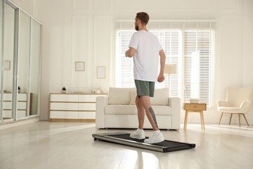 Fototapeta premium Sporty man training on treadmill at home, space for text