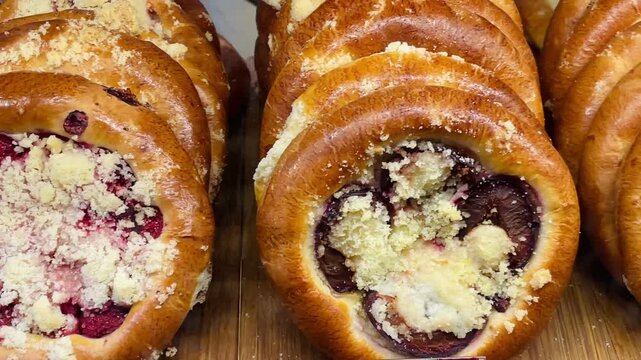 fruit danishes with crumb topping on wooden board, cheese and custard filled rounds beside glossy jam centers and golden brioche edges intimate bakery counter Video taken on mobile device.