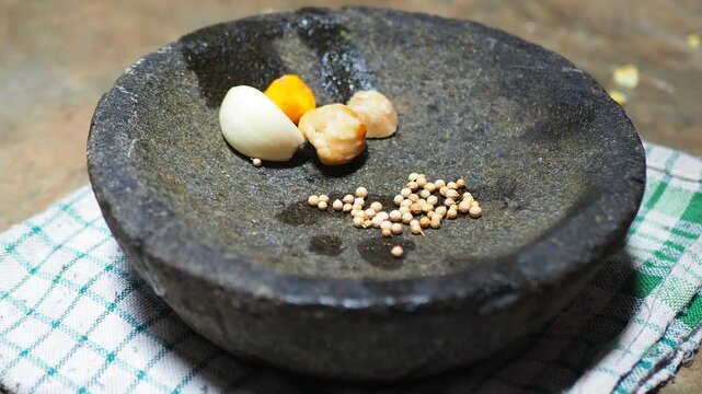 Raw Garlic, Turmeric, Candlenut, and Coriander Seeds in Traditional Stone Mortar for Cooking
