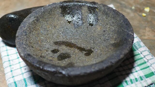 Traditional stone mortar and pestle with residual oil on a checkered cloth, ready for food preparation.